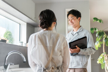 キッチンで主婦に水道屋・設備の説明をする水道屋・設備屋の男性
