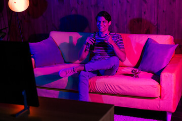Naklejka premium Young man relaxing on sofa with a drink watching TV in a cozy and stylish room