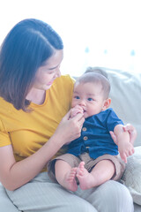 Asian woman with her son holding him by her hand. Happy baby boy was holding by his mother. Asian family with little boy at home enjoy tender family moment, motherhood.