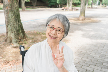 公園で散歩中・気分転換中にピースサインをする優しい笑顔のシニア女性
