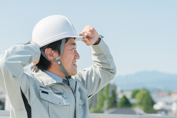 青空の中に立つ作業服を着た作業員（建設・建築・設計・不動産・土木・工事・現場監督・運送）
