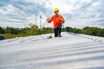 Technician in safety uniform and helmet kneeling on a rooftop, using a drill for precise installation work. A scene highlighting safety, professionalism, and technical expertise in construction.