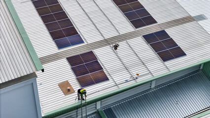 Fototapeta premium technician in safety gear inspects solar panels on a metal rooftop, holding a tool. The scene emphasizes renewable energy, solar technology, and maintenance of sustainable infrastructure.