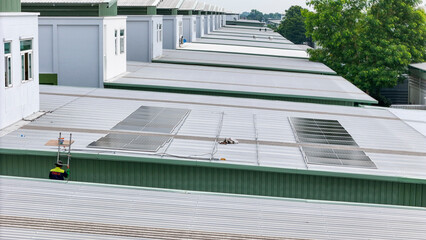 technician in safety gear inspects solar panels on a metal rooftop, holding a tool. The scene...