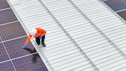 technician in hard hat and safety gear inspects solar panels on a metal rooftop, holding a tool....
