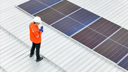 technician in hard hat and safety gear inspects solar panels on a metal rooftop, holding a tool....