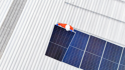 technician in hard hat and safety gear inspects solar panels on a metal rooftop, holding a tool....