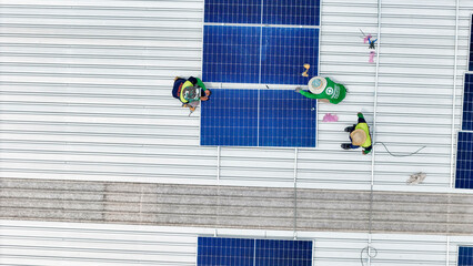 A team of technicians inspects solar panels on metal rooftop, equipped with tools, laptops, and...