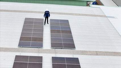 technician in hard hat and safety gear inspects solar panels on a metal rooftop, holding a tool....