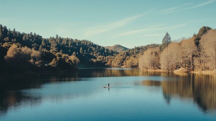 Naklejka premium Serene Kayak Adventure on a Calm Lake Surrounded by Lush Green Trees and Vibrant Autumn Foliage Under Clear Blue Sky in a Picturesque Natural Landscape