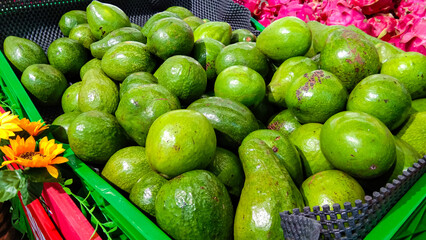 A pile of fresh avocados, in a green basket in a supermarket