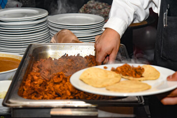 A man is serving food on plates, including tacos and meat