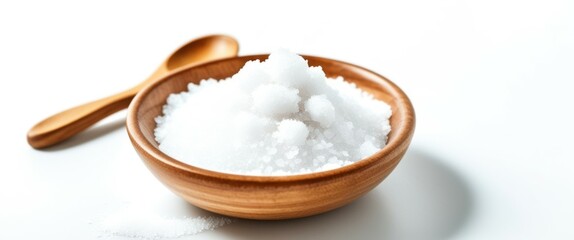A photograph of a wooden bowl filled with white granulated sugar, placed on a white surface. The bowl has a smooth, polished texture and a small wooden spoon resting on the left side. The lighting is 