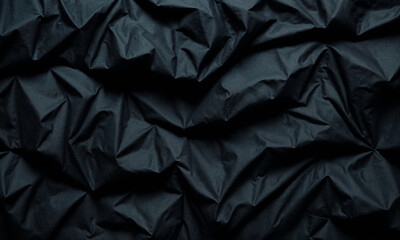 A close-up of black fabric featuring smooth folds and a spiral swirl pattern, creating an elegant and dramatic texture that highlights the simplicity and beauty of dark textiles.