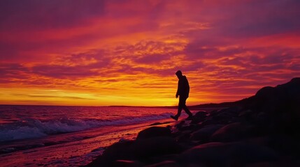 Obraz premium Person walking coast at red sunset with wave action.