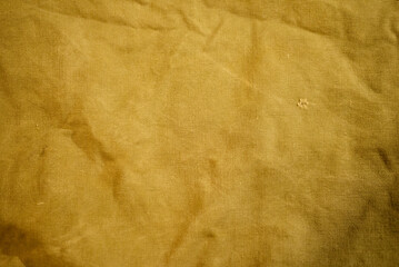 A worn and textured yellow canvas surface with visible imperfections, perfect for artistic or rustic backgrounds.
