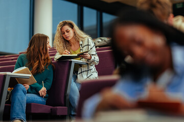University students comparing notes while studying in lecture hall