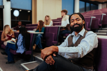 University teacher sitting in lecture hall with students studying behind
