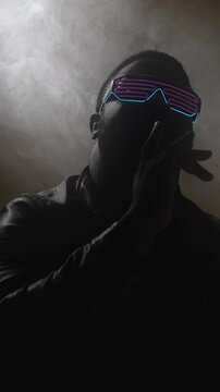 Vertical video. Rap style. Nightclub performer. Modern hip hop artist man in trendy glasses singing song at party show in smoke on dark stage background.