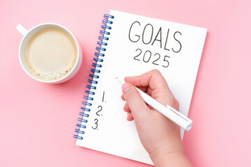 The inscription goals 2025 on notepad and female hand on pink background, top view.