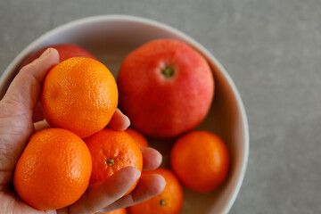 In a bowl, there are tangerines and apples. A hand is holding tangerines.