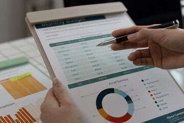A woman is pointing at a graph on a piece of paper. The graph shows a comparison between two sets of data. The woman is using a pen to highlight the differences between the two sets of data
