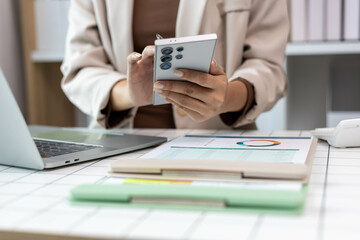 A woman is sitting at a desk with a laptop and a cell phone. She is looking at her cell phone while sitting at the desk