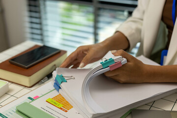 A woman is holding a stack of papers on a desk. The papers are organized and labeled with different...