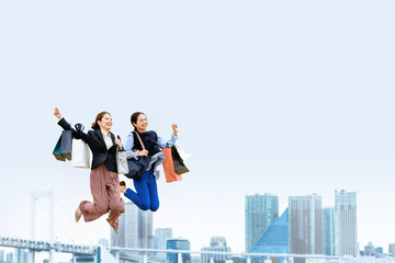 買い物袋を沢山持ってジャンプする女性2人（セール・爆買い）