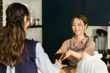 Obraz premium カフェでスマホ決済をする女性（飲食店・テイクアウト）