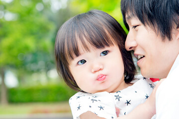 新緑の樹木を背景に父と一緒に遊ぶ幼い女の子。父子,愛情,育児のイメージ