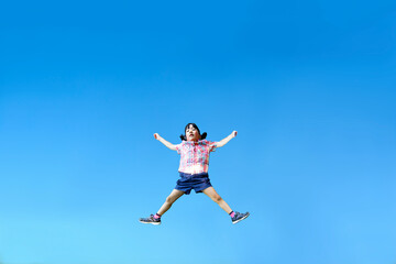 青空を背景に手足を広げジャンプをする幼い女の子1人