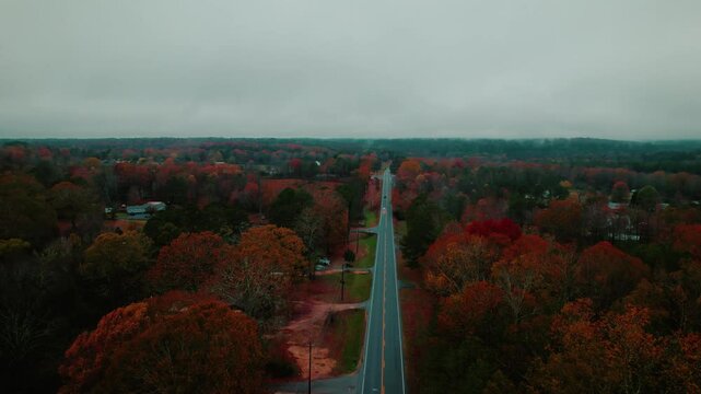 Drone view of a conestoga semi truck traveling along a quiet rural road, surrounded by colorful autumn trees in Fort Payne, Alabama.