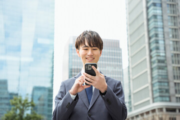 都会の屋外で両手でスマートフォンを操作する20代から30代のスーツ姿の男性