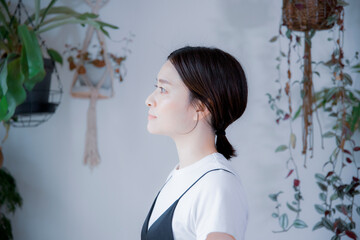 明るい植物のある室内でどこかを見つめるワンピース姿の日本人女性