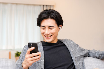 自宅のリビングでスマートフォンを笑顔で操作する30代の男性