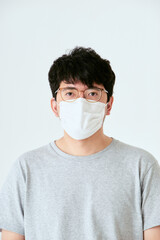 白背景でカメラ目線のマスクと眼鏡を着けた30代の1人の日本人男性の人物の上半身の正面