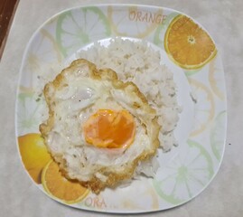 Thai deep-fried egg on top of jasmine rice in plastic plate servers on wood table