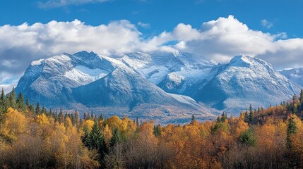 Majestic snow-capped mountains rise above vibrant autumn foliage under a blue sky.
