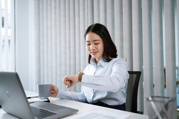 Portrait of  Asian Business woman watching at wristwatch while working on laptop computer in office. watching the time .working new start up project