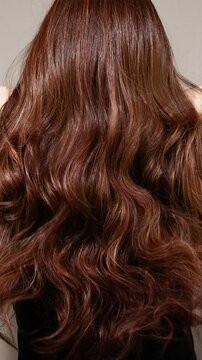 Vertical closeup young woman model long brown curly hair texture in slow motion