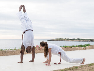 Two people practicing capoeira on a scenic outdoor terrace near the ocean