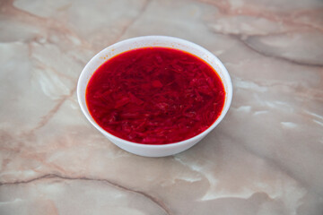Red borscht in a white bowl on a marble background.