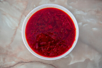 Red borscht in a white bowl on a marble background top view