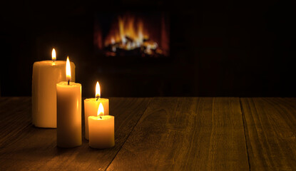 IMAGE BACKGROUND WITH LIT CANDLES ON THE WOOD TABLE IN THE FOREGROUND AND FIREPLACE IN THE BACKGROUND