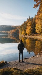 Rear view of a man standing by a calm lake in autumn