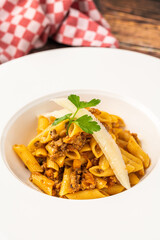 Top view of penne bolognese pasta in white plate on wooden table