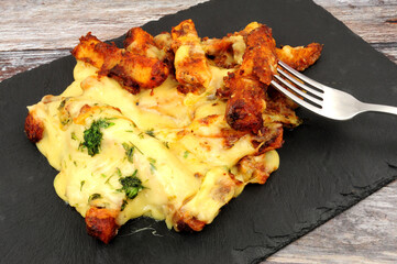 Portion of dirty cheesy fries on a slate serving board, fried battered skin on potato chips topped with Monterey jack cheddar cheese, bacon sauce and mozzarella and jalapenos