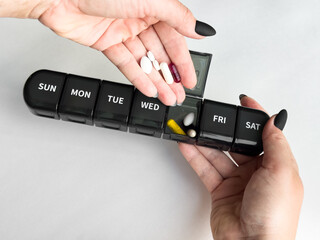 Weekly pill organizer: woman taking medication with daily compartment in hand