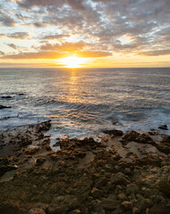 Golden sunset in south of Tenerife, Atlantic ocean waves crash on the rocky beach, horizon over water